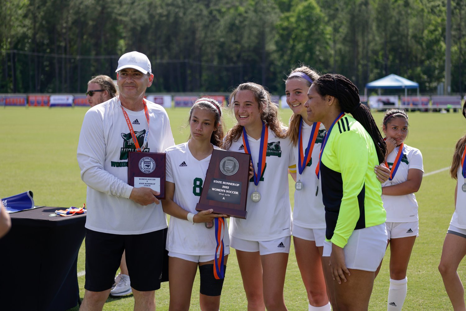 A few members of Woods Charter's women's soccer team (from left to right: head coach Graeme Stewart, sophomore Leyla Noronha, junior Chloe Richard, junior Lucy Miller, senior Jana Matthews) pose with the 1A runner-up trophy after the Wolves' 3-0 loss to the Christ the King Crusaders in the 1A state title game last Saturday in Cary.